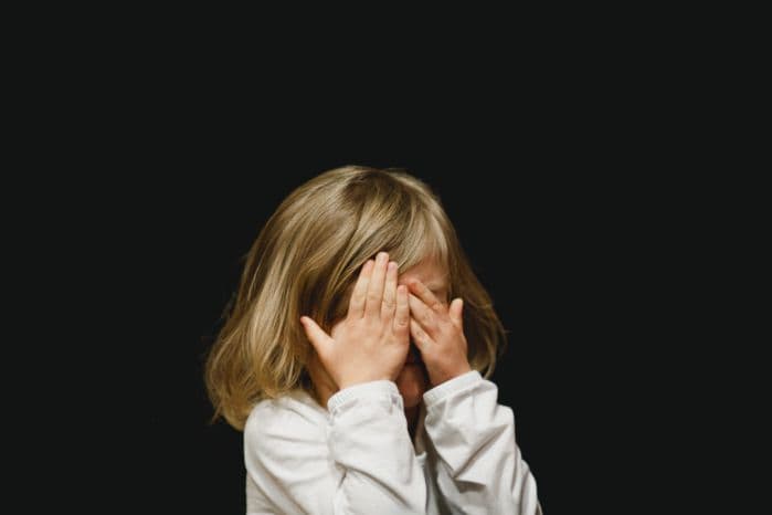 Menina com as mãos no rosto como se sentisse vergonha