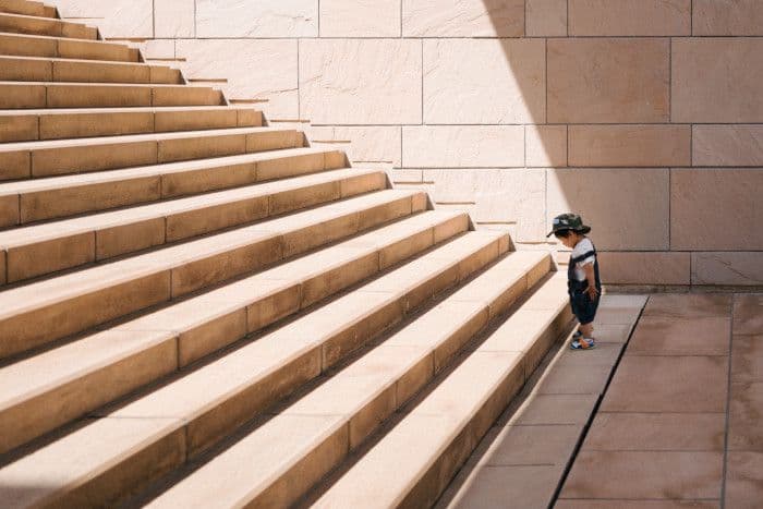 Imagem de um bebê encarando uma grande escadaria antes do primeiro degrau