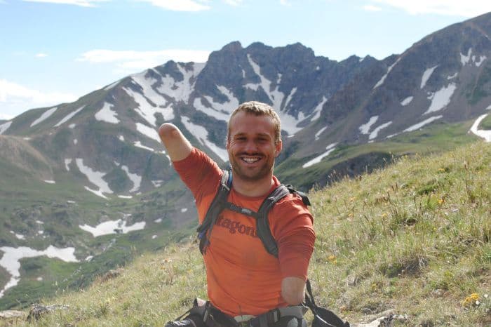 Segunda imagem que mostra Kyle Mainard sem braços em cima de uma montanha
