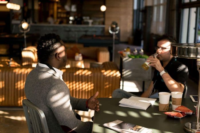 Dois homens conversando e sentados em uma mesa.