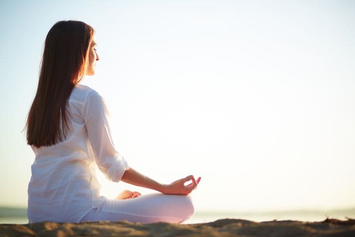 Mulher sentada ao chão meditando de costas para a tela