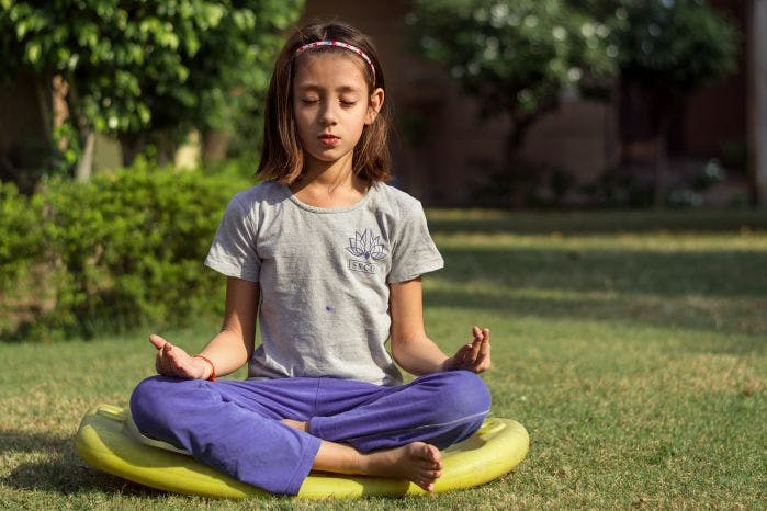 garotinha sentada com as pernas cruzadas na posição de meditação tradicional