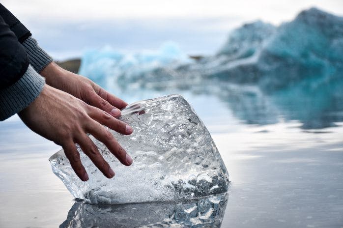 mãos encostando em um grande pedaço de gelo